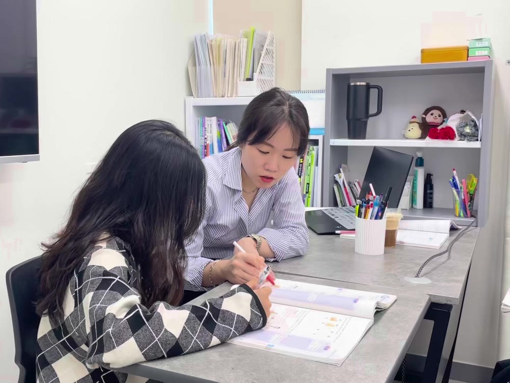 선생님이 학생과 마주 앉아 문제집을 짚어 가며 설명하는 1:1 피드백 장면